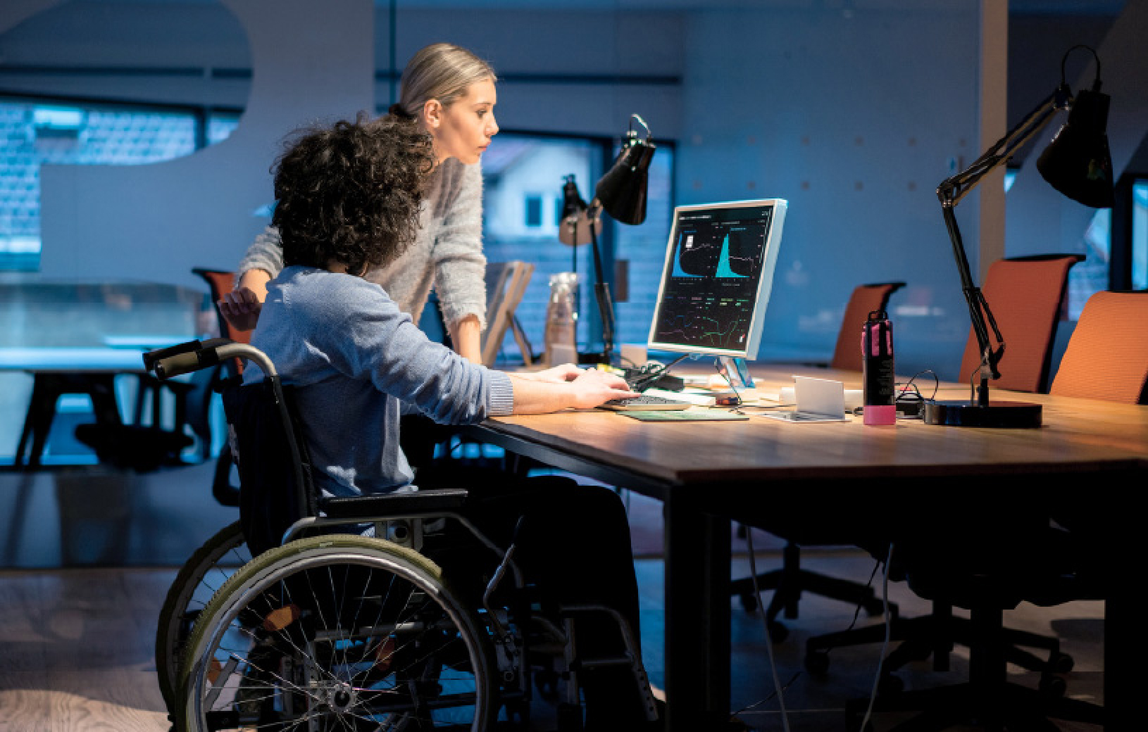 Photo d'illustration : Un jeune homme est assis dans un fauteuil roulant devant un ordinateur qui affiche des graphiques. Il est accompagné d'une jeune femme qui regarde également l'écran. Valorisation de la donnée. Données de santé. Souveraineté numérique. Parcours patient. Parcours santé. Parcours de soin.