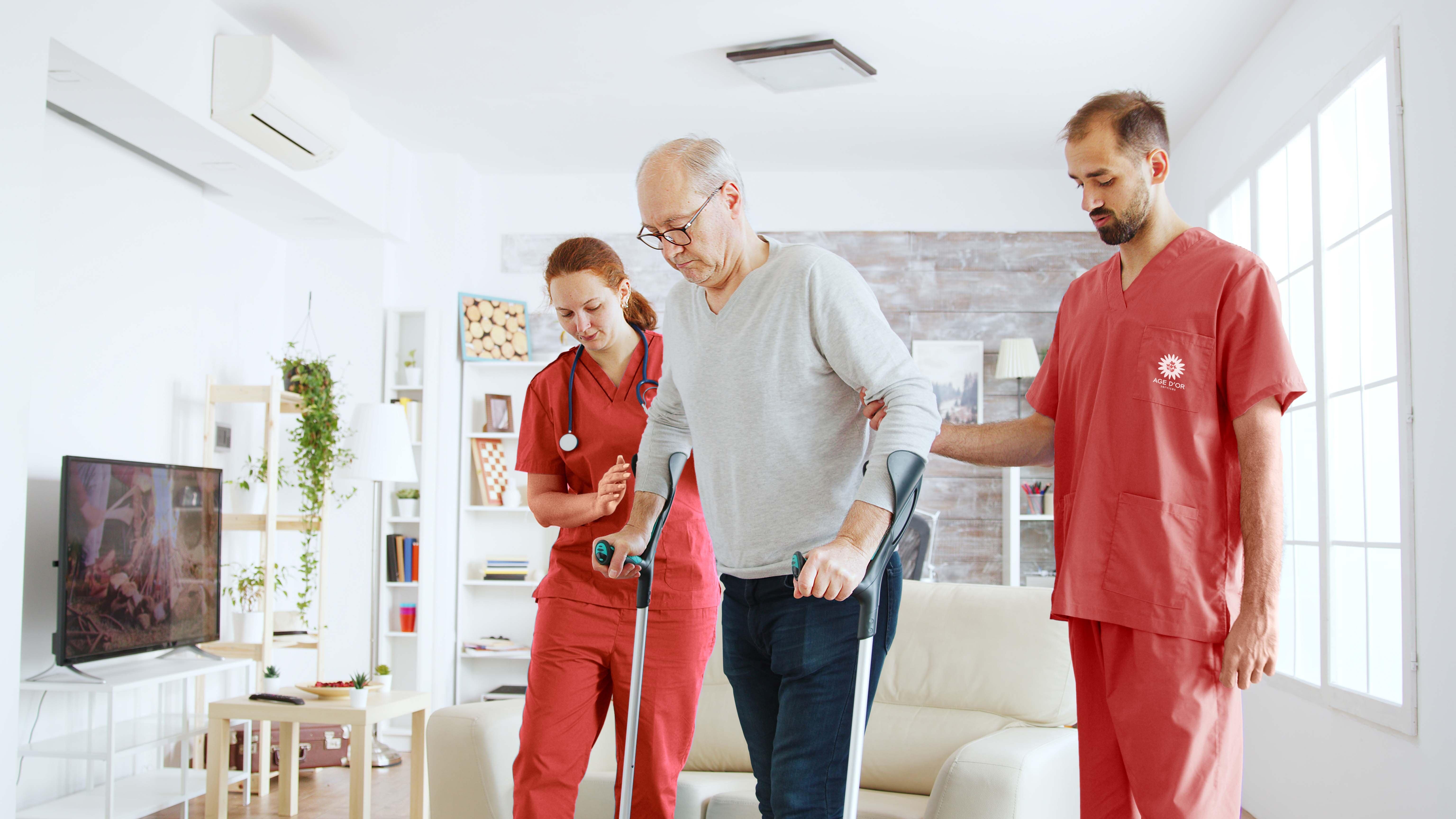 Photo d'illustration Axéo Services : Deux infirmiers à domicile aident un patient à marcher avec des béquilles. Soins à domicile, Parcours santé. Parcours de soin. Autonomie